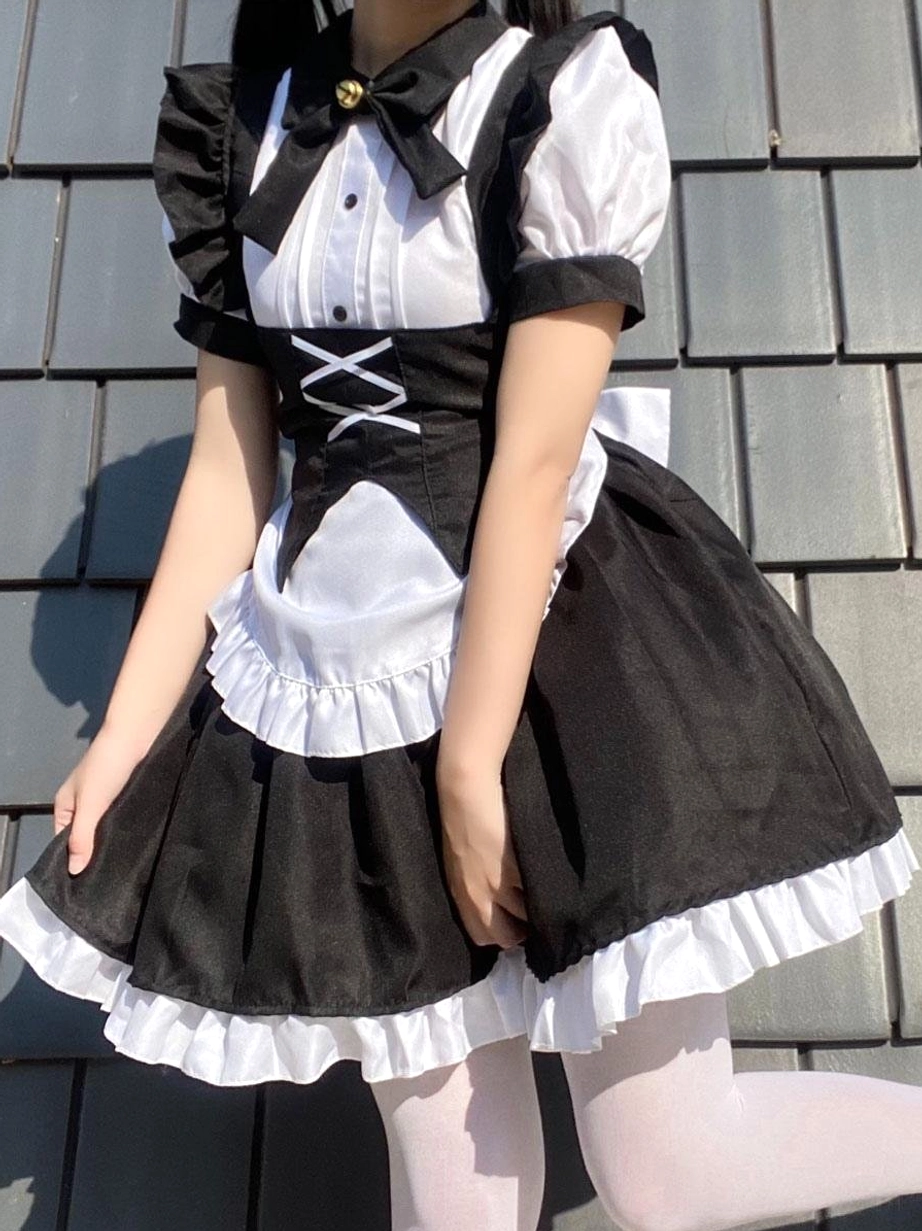 Gothic black maid lolita dress front view on model with lifted leg wearing white stockings, featuring back bow decoration, ruffled hem edge, and classic lolita silhouette