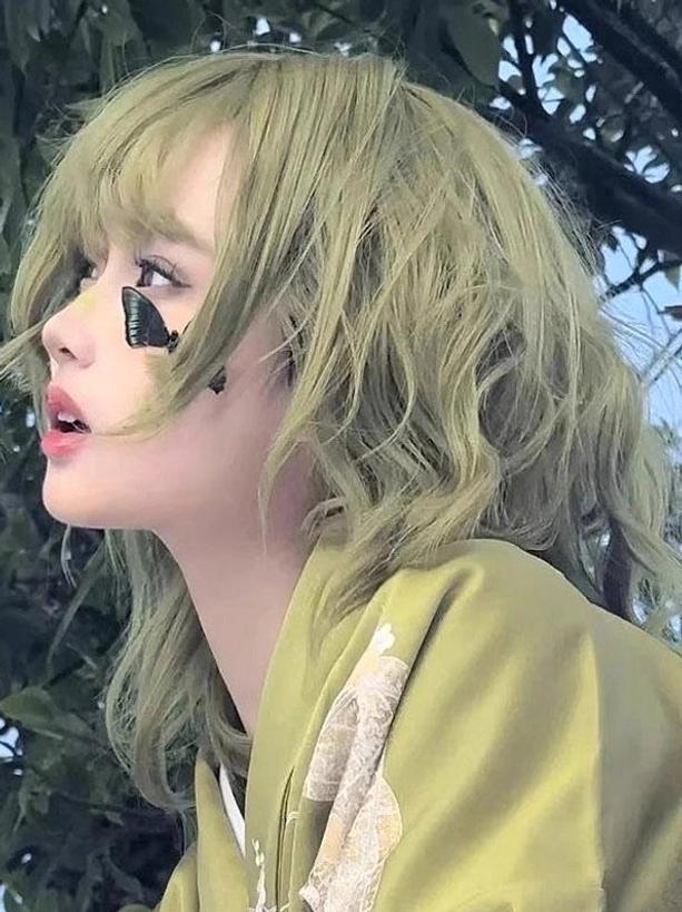 Matcha green short wavy lolita wig with air bangs, left profile close-up view outdoors showing delicate wavy texture and soft framing