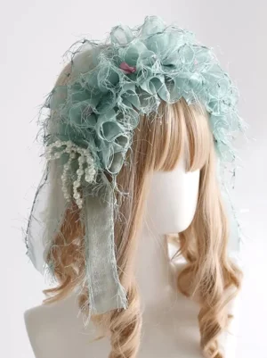 Mint green sweet lolita headdress with frayed organza ruffles and pearl tassel decor featuring tiny pink accents, displayed on blonde wig from three-quarter angle