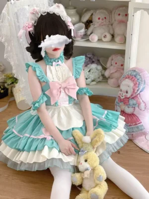 Mint green sleeveless maid-style sweet lolita dress with pink-white color block design, large front bow, multi-layer ruffled skirt, worn by model with maid hair ornaments sitting in cute doll bedroom