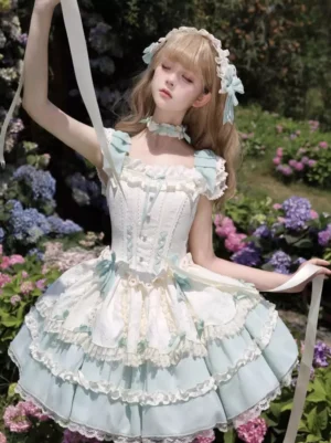 Mint green and off-white sweet lolita dress with lace-up front bodice, layered ruffles, and satin bows, worn by blonde model in outdoor flower garden setting, sleeveless design with front high-angle view