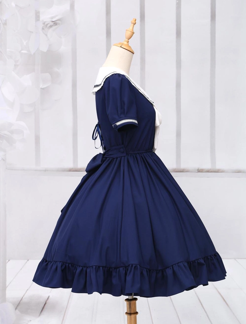 Navy sailor lolita dress left-side full view on dress form, visible back bow and ruffled hem silhouette