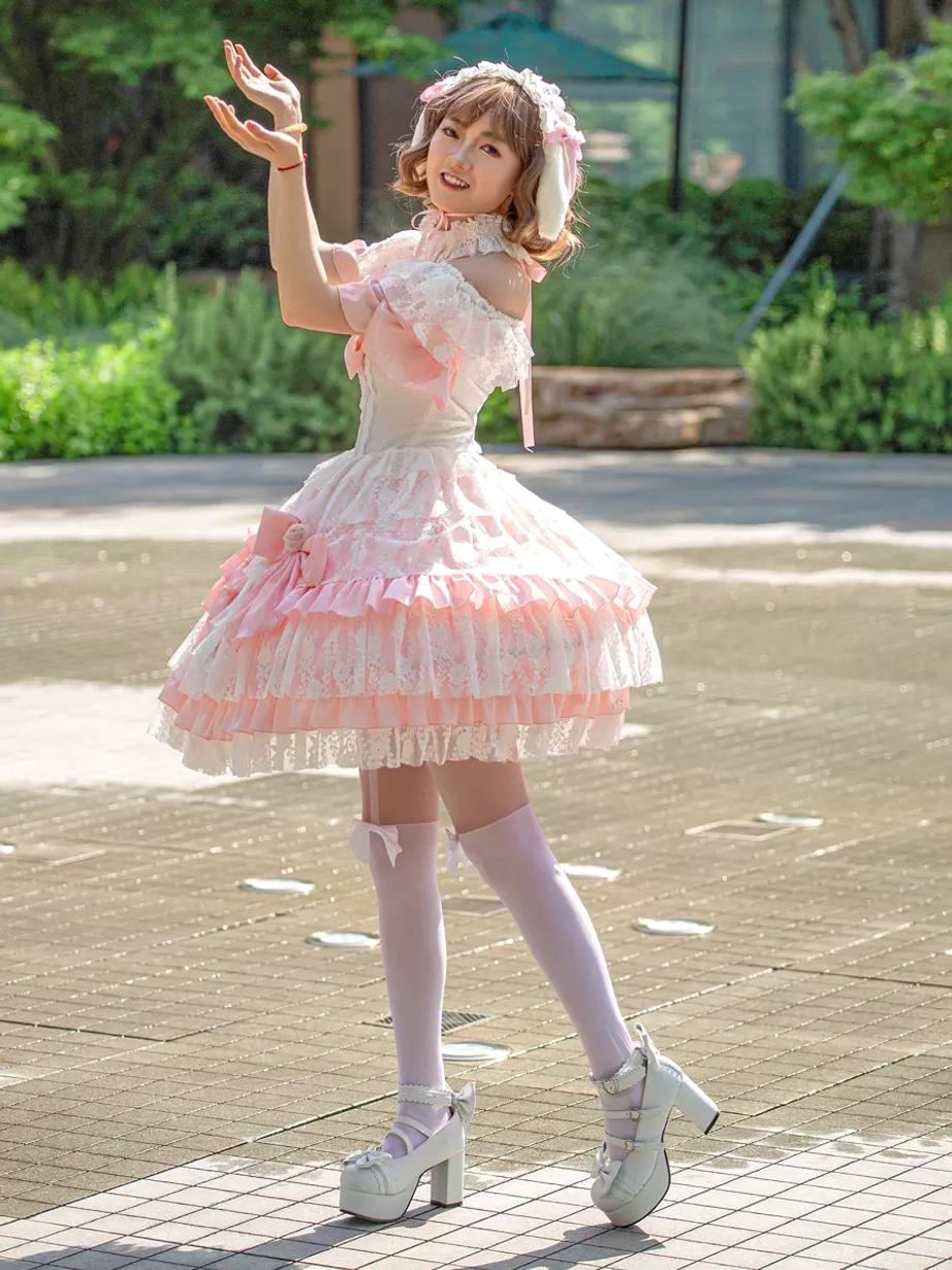 Off-shoulder pink sweet lolita dress side-back view with white platform heels and layered lace skirt outdoor plaza