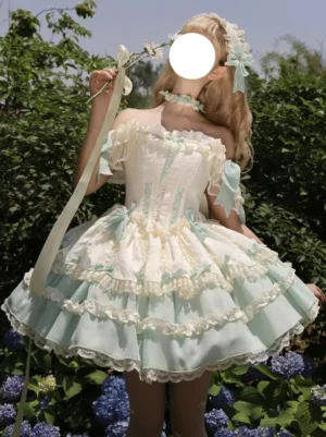 Off-shoulder sweet lolita JSK dress with tiered ruffle skirt and corset waist in mint green and cream, front three-quarter view worn outdoors in garden setting with lace trims and hanging ribbons