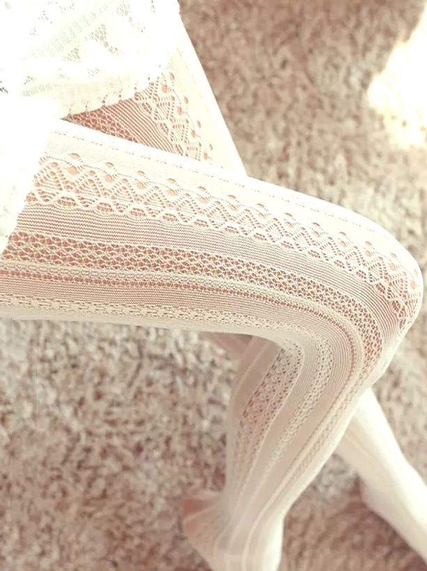 Off-white delicate lace cut-out lolita tights with vertical floral hollow pattern close-up detail on leg showing sheer embroidered fabric texture and romantic aesthetic