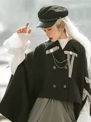 Ouji gothic lolita cape three-quarter front view with pearl chains and velvet bows, model wearing newsboy cap with long white hair and ruffled blouse