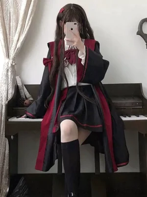 Gothic Ouji Lolita academy style ensemble with hoodless long cape, bow necktie blouse, and accordion pleated mini skirt - sitting pose beside vintage piano showing detailed tailoring