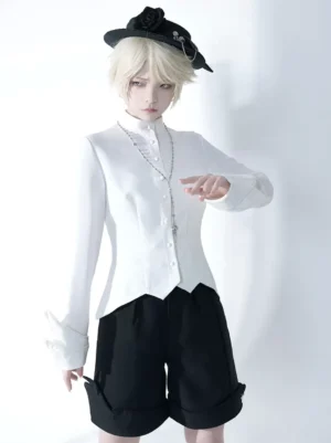 Ouji Lolita formal white blouse three-quarter front angle showing decorative long cuffs, pointed shirt hem, and aristocratic silhouette with black loose shorts and cross necklace accessory