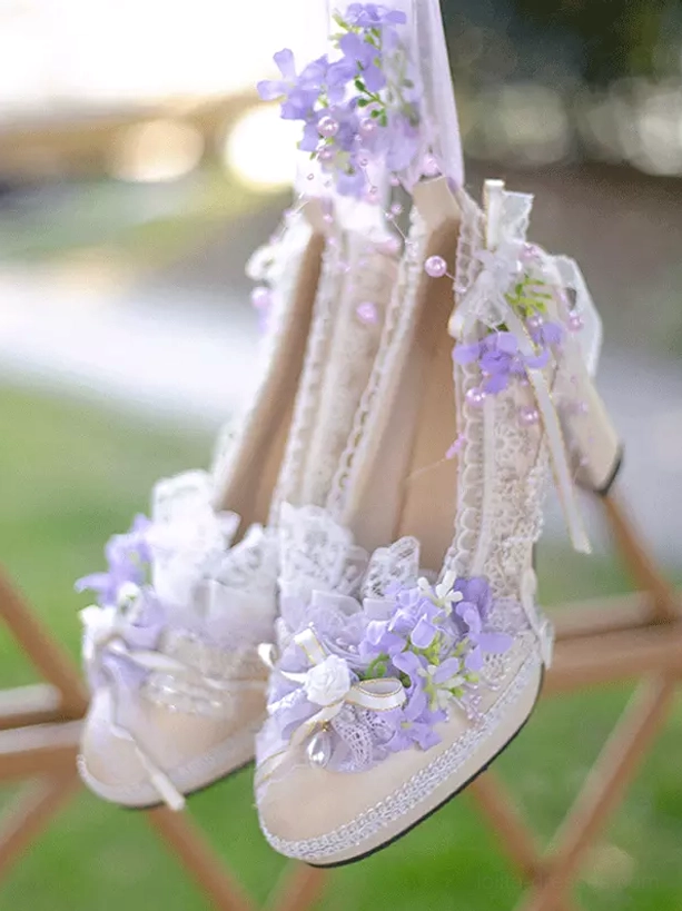 Pair of purple Lolita pumps with ornate floral decoration and lace straps showing pearl bead accents displayed from side overhead view on wooden display rack