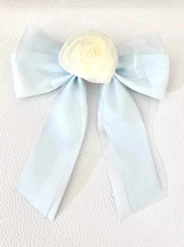 Pale blue sheer organza bow hair clip with cream rose decoration, flat lay front view on white textured background, serene pastel sweet lolita hair accessory