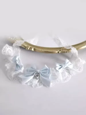 Pastel blue sweet lolita choker with white lace frills and heart gem pendant displayed on golden mirror frame flat lay, showing intricate bow details and satin finish