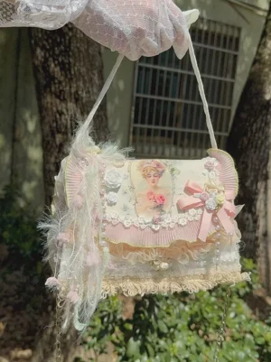 Pink-white pastoral lolita crossbody bag with vintage lady appliqué and ruffled trim, held by gloved hand outdoors with green foliage background, featuring delicate bow and feather embellishments for sweet lolita coordinate