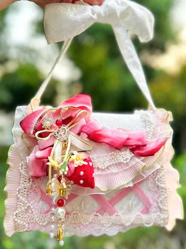 Pastoral lolita cross-body handbag with white bow shoulder strap, ruffled lace trim, strawberry pendant, and pearl tassel decor held in garden setting overhead front view