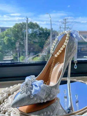 Side profile of glitter bridal stiletto heels featuring pearl ankle chain crystal drop pendant blue tulle bow and silver glitter upper