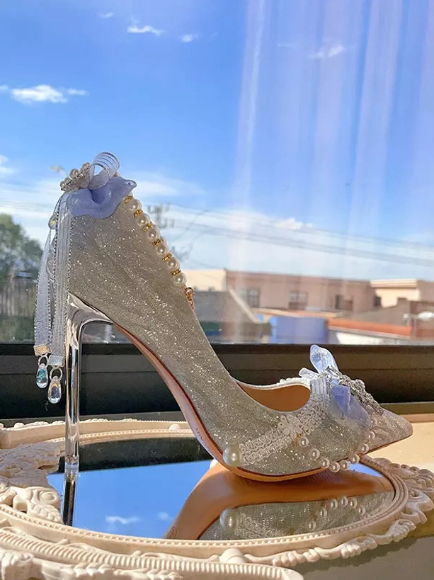 Side profile stiletto heel with pearl ankle strap crystal heel pendant blue bow decor and silver glitter fabric upper on windowsill