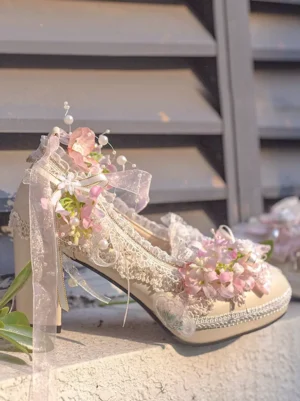 Single Lolita high heel pump with pink floral accents featuring intricate lace detailing and pearl ornaments shown from side oblique view on outdoor stone steps backdrop