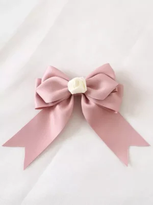 Pink bow sweet lolita headdress flat lay detail view showing double-layer satin construction, fishtail ribbon tails, and cream rose center ornament on white background, close-up product photography