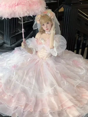 Pink fairy Lolita wedding dress with spaghetti strap puff sleeves, corset waist, and sheer tiered tulle skirt, medium shot of blonde model holding pink feather umbrella on indoor staircase