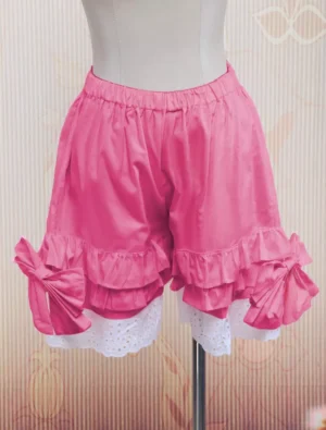 Soft pink cotton lolita bloomers with white lace ruffled hems and decorative side bows, displayed on torso mannequin showing front left three-quarter angle view against vintage backdrop