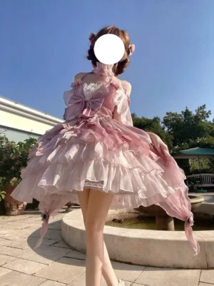 Pink fairy lolita gown rear back view showing large back bow decoration and irregular trailing tulle hem with flower hair accessories in fountain courtyard