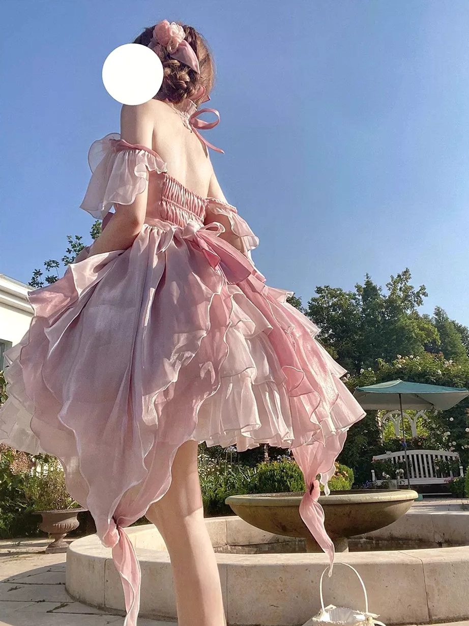 Pink fairy lolita gown low-angle rear full view with bare back halter neck tie fastened at back and pink flower hair accessory in fountain courtyard