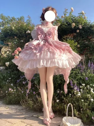 Pink fairy lolita princess gown full front view with gradient ruffled layered skirt and oversized front bow choker detail outdoors in flower garden setting
