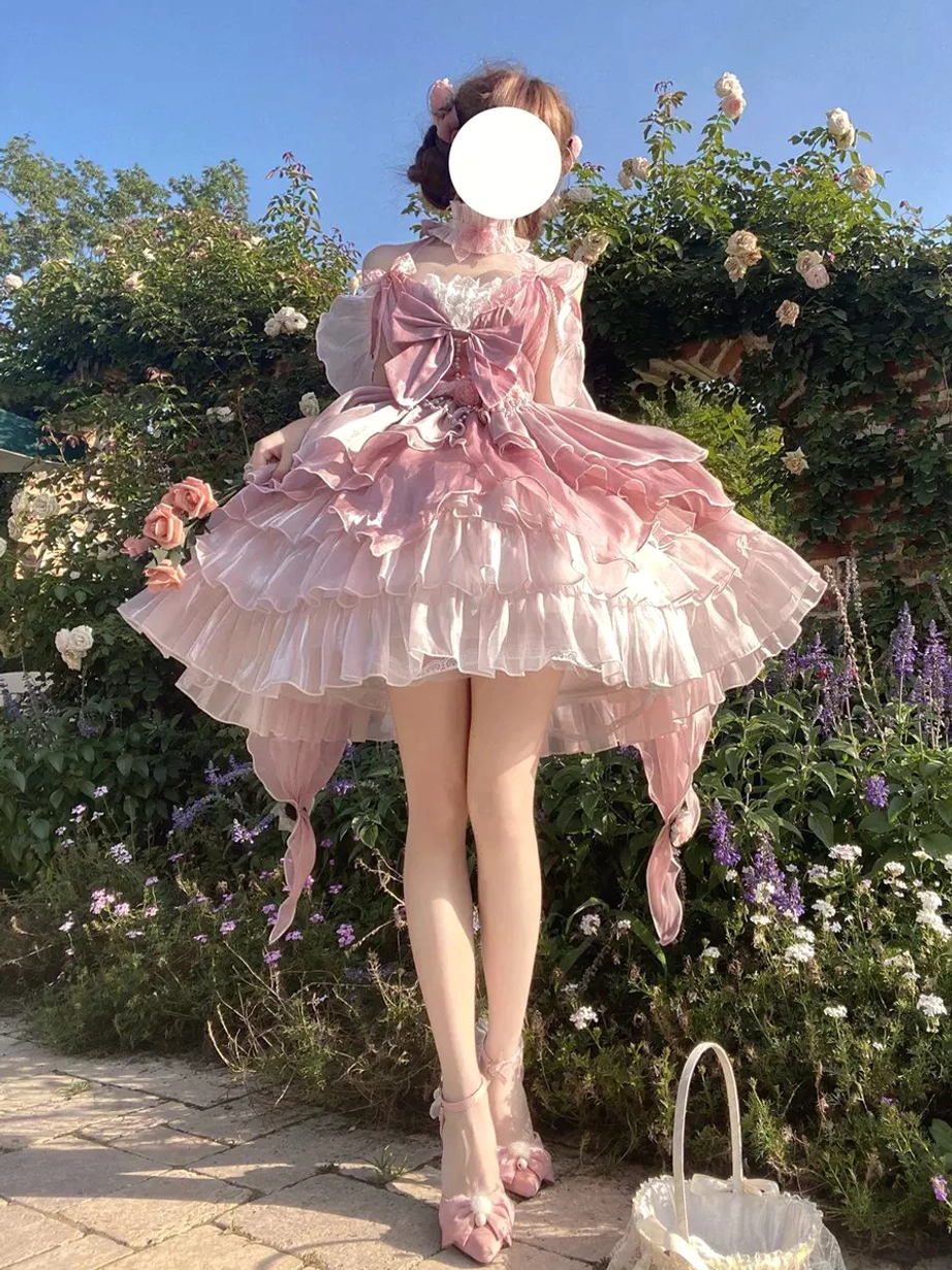 Pink fairy lolita princess gown full front view with gradient ruffled layered skirt and oversized front bow choker detail outdoors in flower garden setting