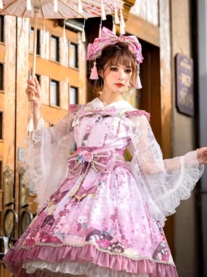 Pink floral kimono lolita jsk dress with matching headwear featuring sheer lace sleeves and large waist bow, front three-quarter view worn by model at traditional Japanese doorway