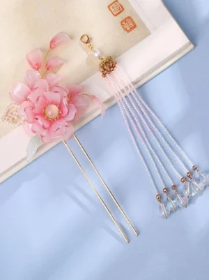 Flat lay top view of pink flower tassel hairpin featuring layered resin flowers long glass bead tassel gold decorative hardware and crystal drop pendants on blue table with vintage book backdrop