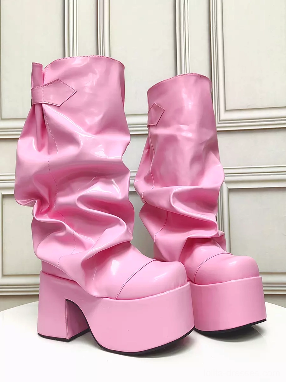 Pair of pink slouchy platform Gothic Lolita boots front three-quarter view with high gloss pink PU leather and ruched shaft against paneled wall background