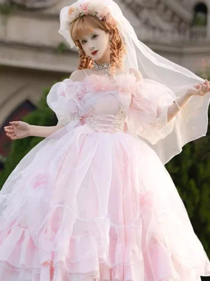Pink bridal Hime Lolita jumper dress with off-shoulder puff sleeves and layered ruffled tulle skirt, front full-body view worn by blonde model with wedding veil in European garden setting