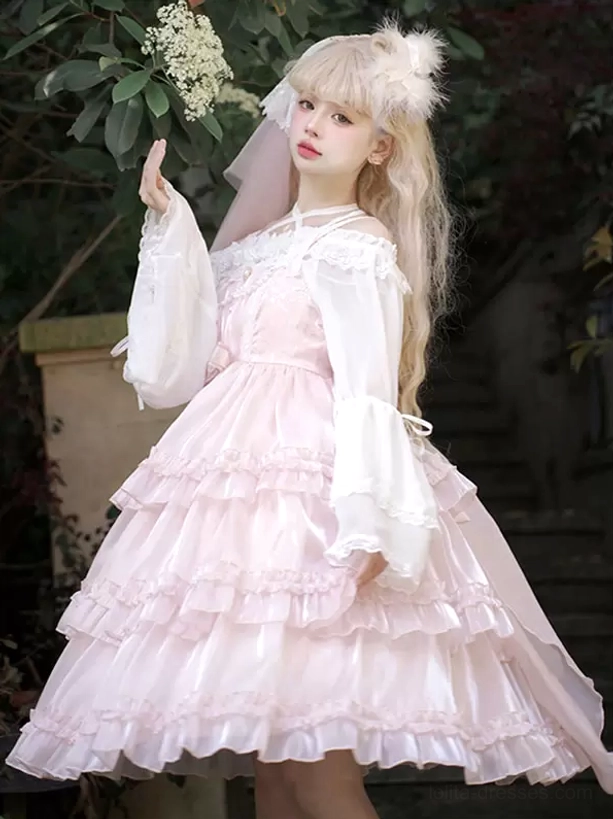 Pink sweet Hime Lolita jumper dress right three-quarter angle showing flare long sleeves detail, glossy pink fabric, fluffy hair accessory, outdoor flower courtyard setting