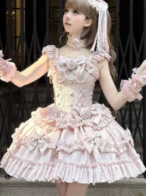 Pink Hime Lolita jumper dress front three-quarter view worn by model outdoors with iron fence background, showing ruffled straps and multi-layer ruffled skirt details