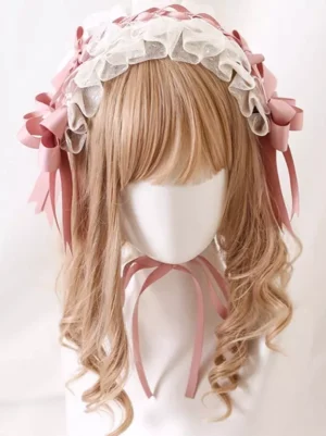 Pink lace lolita headdress with white ruffled trim and layered pink satin bows featuring long ribbon streamers, displayed on light brown curly wig mannequin front view