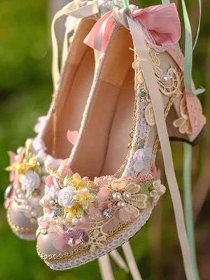 Pink lace pearl floral bridal block heel lolita shoes front oblique view showing delicate lace overlays ruffled details and sparkling gemstone embellishments on outdoor grass background