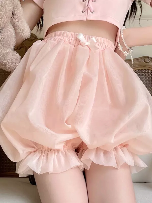 Pink lolita bloomer shorts close-up front view with ruffled hem decorative waist bow vintage indoor setting pearl bracelet accessory