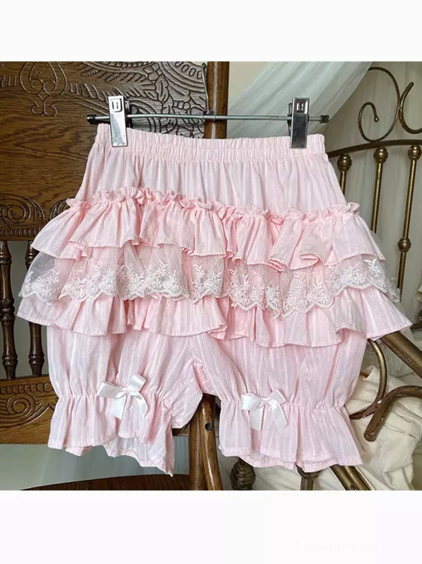 Pink lolita bloomers flat lay hanging garment with lace-trimmed layers elastic waist and bowknots on leg cuffs vintage bedroom background