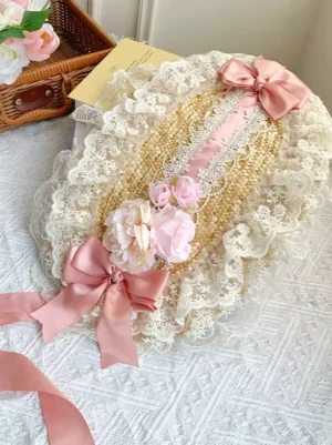 Pink and cream Lolita bonnet headdress featuring delicate lace ruffles and pink satin bows with straw woven base detail on pastoral studio setup