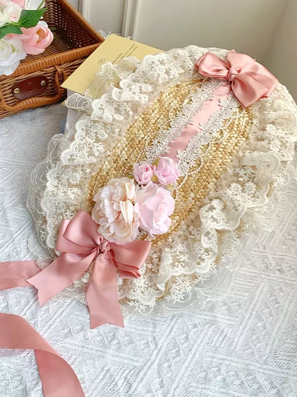 Pink and cream Lolita bonnet headdress featuring delicate lace ruffles and pink satin bows with straw woven base detail on pastoral studio setup