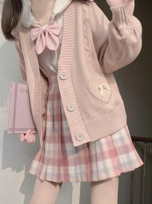 Pink lolita sweater cardigan with heart bow pockets and cable knit texture worn by model holding notebook in three-quarter view