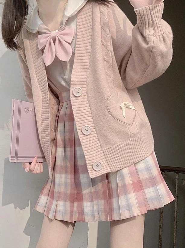 Pink lolita sweater cardigan with heart bow pockets and cable knit texture worn by model holding notebook in three-quarter view