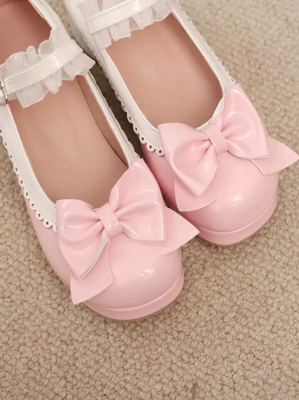 Flat lay overhead view of pink Lolita chunky heel pumps showing prominent front bows, ruffled ankle strap, patent leather glossy finish on textured carpet