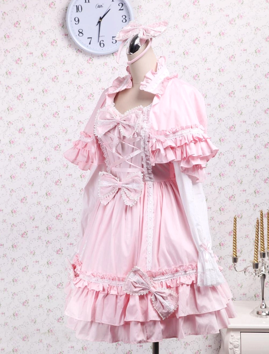 Right side view of pink lolita dress capelet set on dress form showing bow details waist skirt sheer long sleeves and studio setting