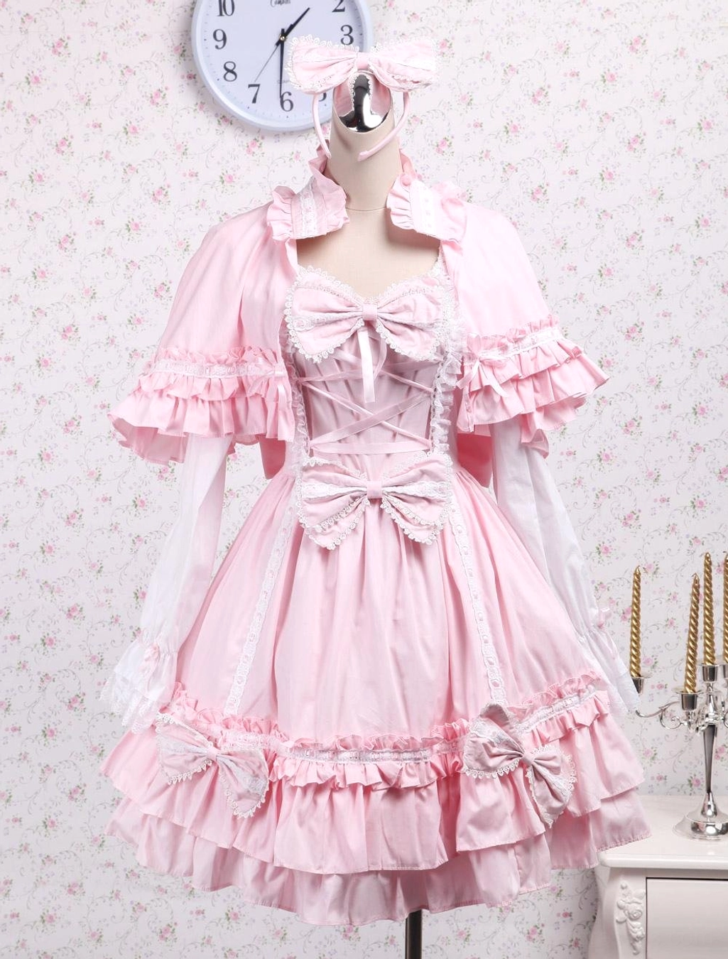 Pink lolita dress and ruffled capelet set on dress form showing corset waist multiple bow accents lace trims and tiered ruffles