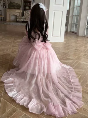 Back view of pink sweet lolita dress showing large bow decoration and cascading ruffled tulle train with off-shoulder silhouette