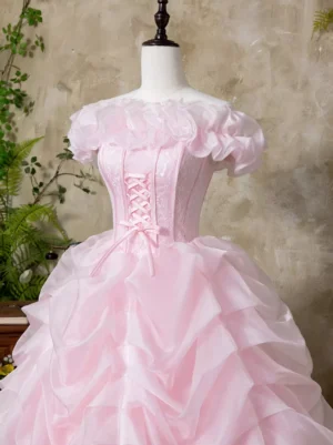 Close-up front view of pink Lolita dress featuring detailed ruffled off-shoulder trim and structured lace-up corset bodice with layered ruched skirt against vintage textured wall