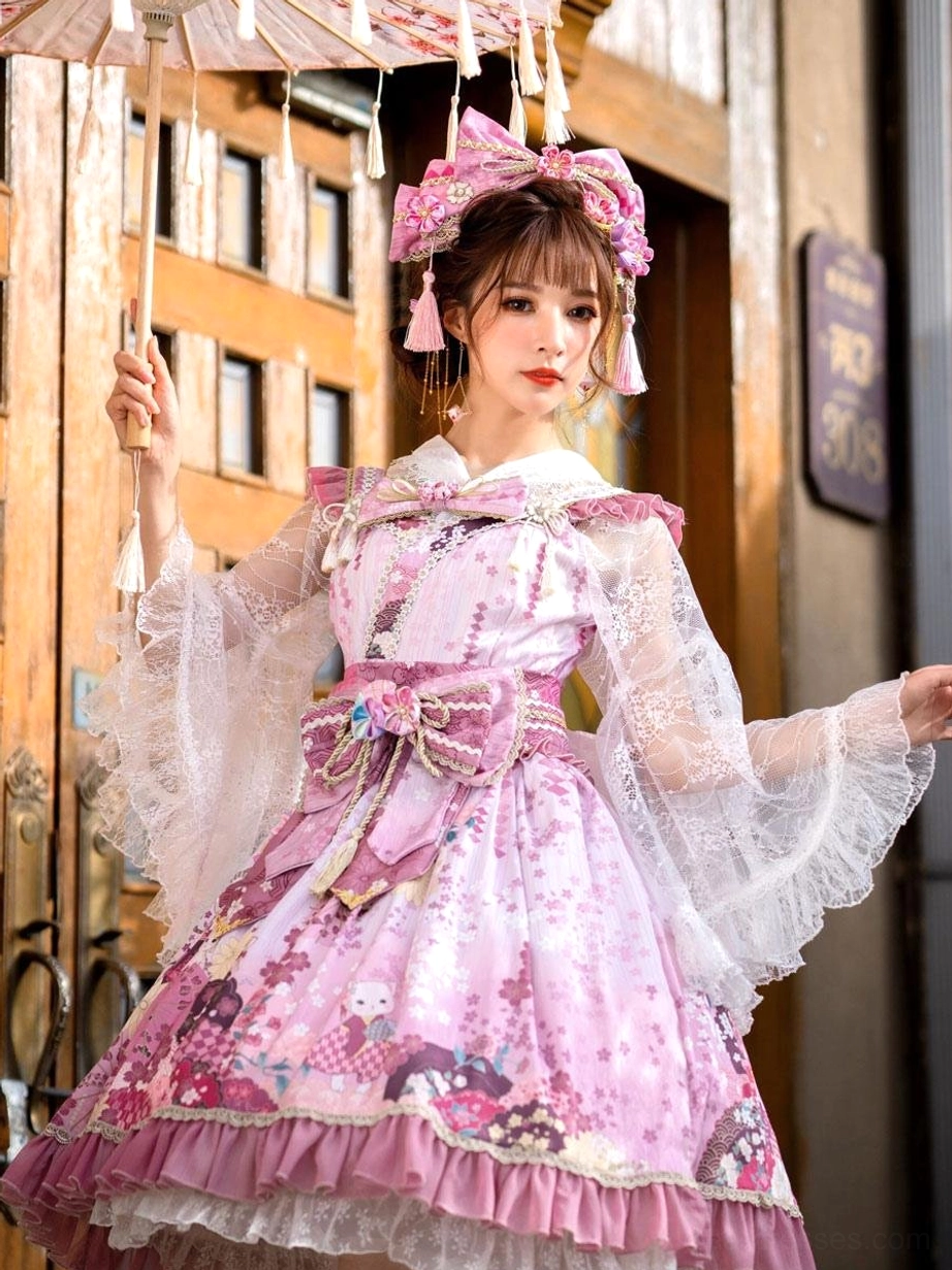 Pink lolita dress with sheer lace sleeves ruffled hem full-body front view near wooden vintage building with matching head and waist bow