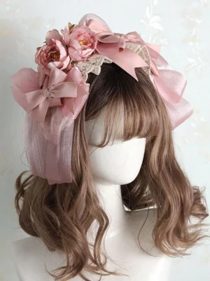 Pink Lolita headdress with oversized dusty pink bows and peony flowers displayed on mannequin wearing brown wavy wig, left front three-quarter view showing satin bows, fabric flower details, delicate lace trim and sheer pink tulle layering typical of Sweet Lolita fashion aesthetic
