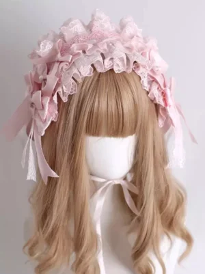 Front view of pink lolita headpiece on long blonde curly wig mannequin, displaying full ruffled lace construction with satin bow embellishments and neck fastening ribbon ties