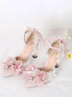 Pink pointed-toe Lolita high heel sandals with organza butterfly bows and rhinestone pendants, displayed at oblique angle on white floral fabric background, showing delicate ruffled mesh trims and ankle buckle straps in Sweet Lolita style